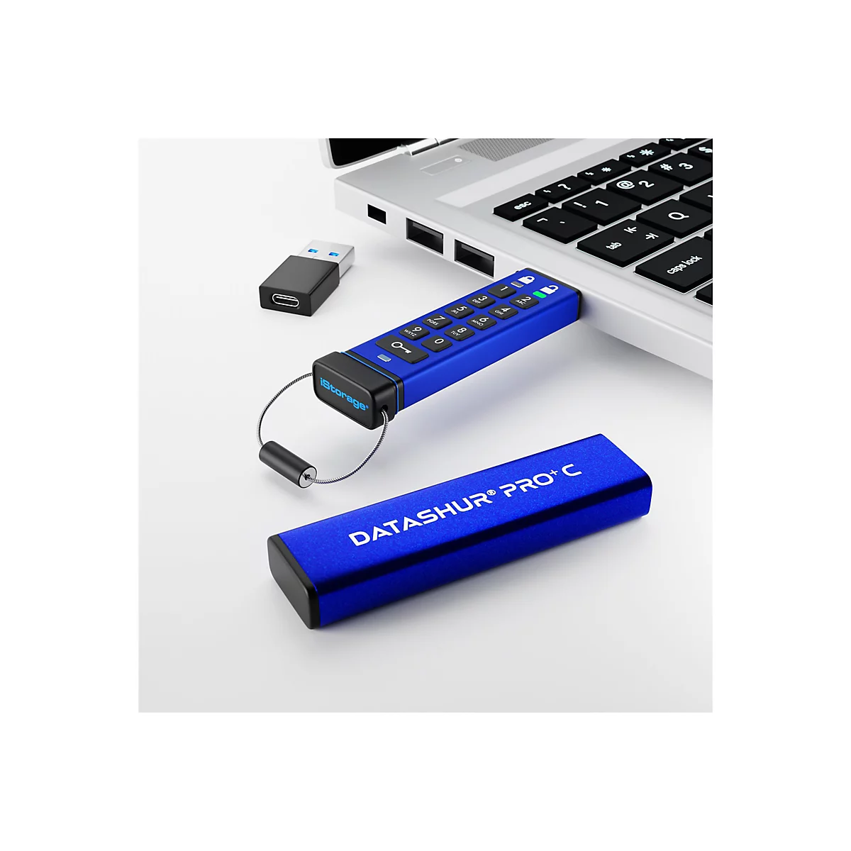 Blauer USB-Stick mit Tastatur und Metall-Schlaufe, neben einem Laptop und einem weiteren Stick. Auf dem Stick steht "DATASHUR PRO+ C".