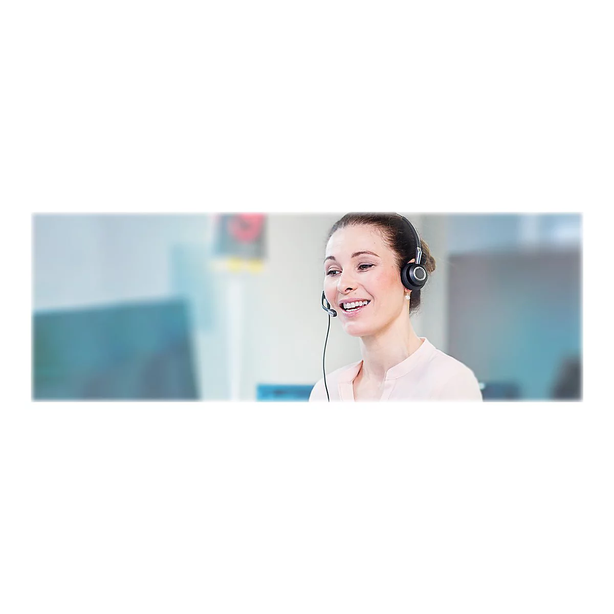 LÃ¤chelnde Frau mit Headset. Sie sitzt am Arbeitsplatz, wahrscheinlich im Kundenservice.