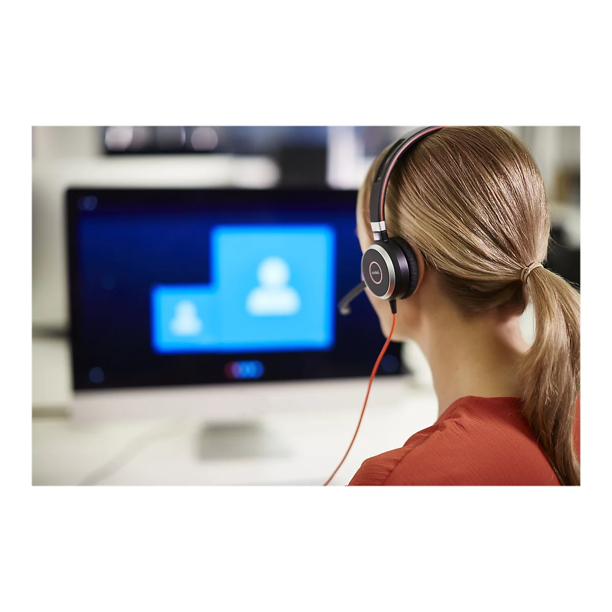 Eine Person mit Headset, die vor einem Bildschirm sitzt, an einem Videoanruf teilnimmt.
