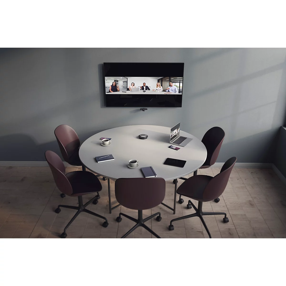 Ein runder Konferenztisch mit Stühlen in einem modern eingerichteten Büro mit Videokonferenzbildschirm an der Wand.