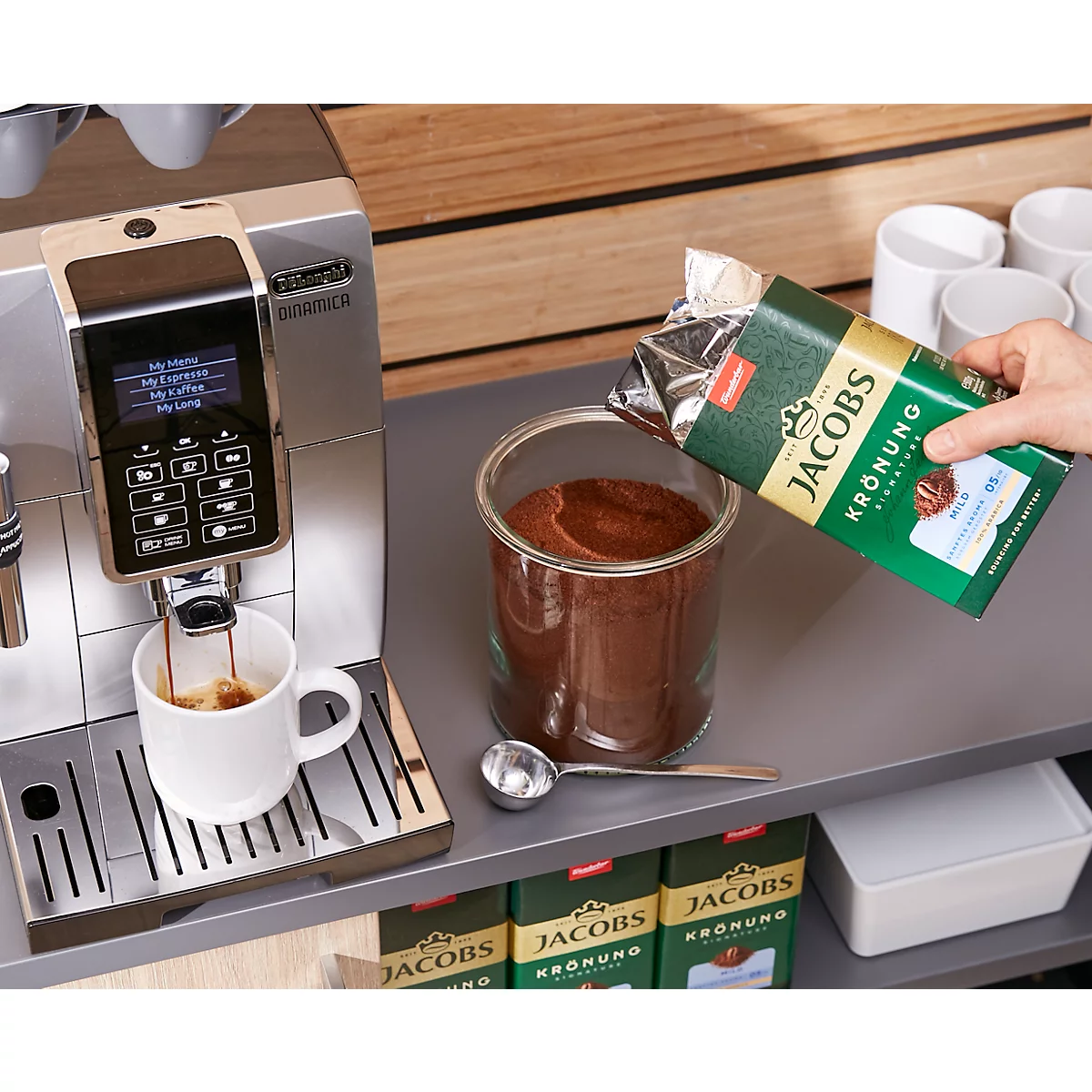 Koffiemachine met koffie die in een kopje giet. Persoon giet koffiepoeder in een glas. Jacobs Krönung koffieverpakking.
