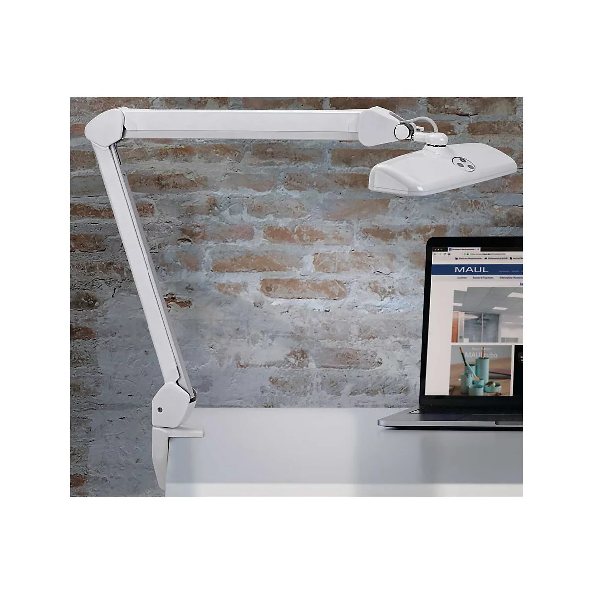 Weiße Schreibtisch-Klemmlampe mit Gelenkarm vor einer Backsteinwand neben einem Laptop.