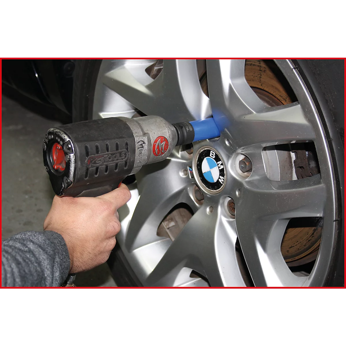 Une personne dévisse une roue avec une clé à chocs. Jante argentée avec logo BMW.