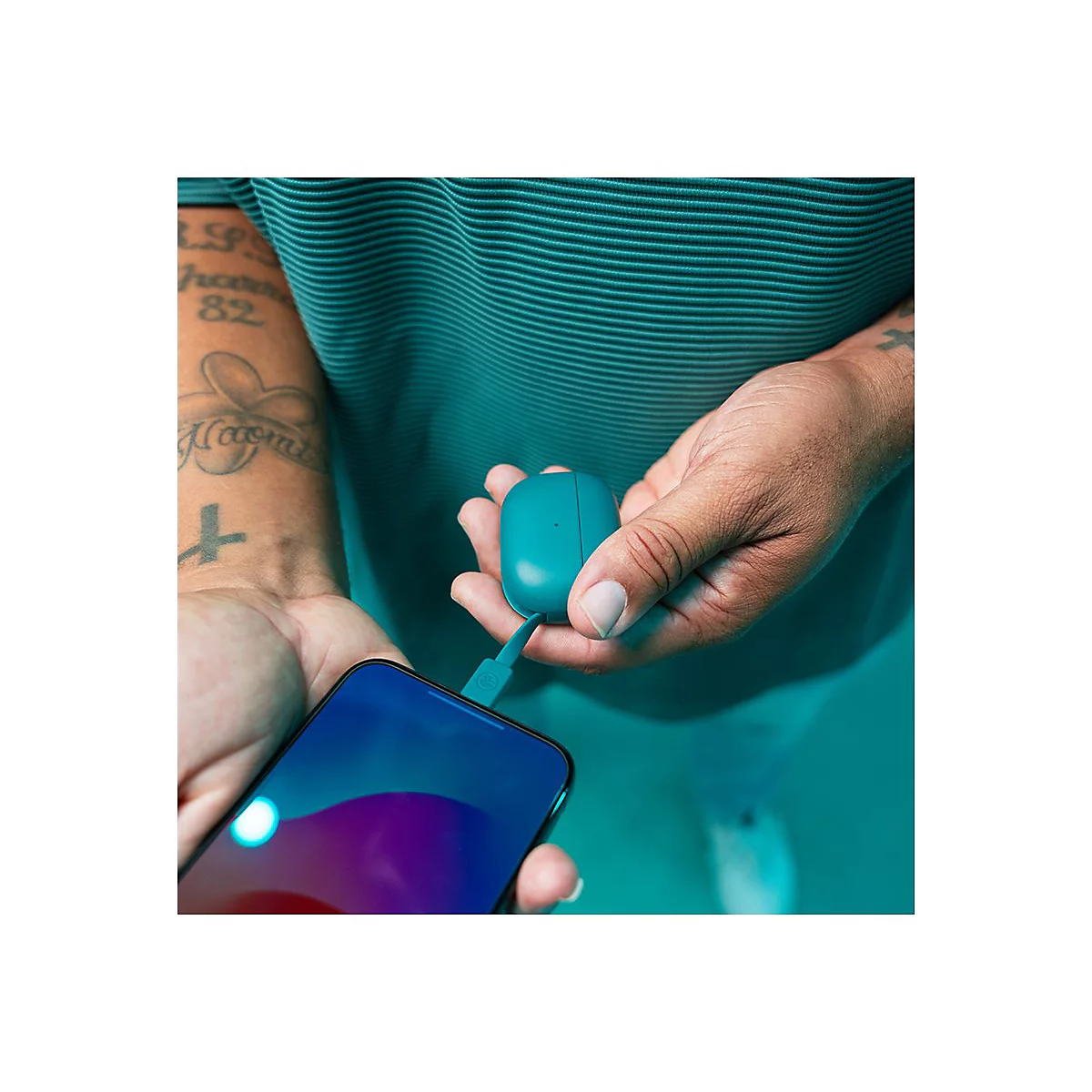 Personne tenant un étui de chargement bleu et un smartphone avec un câble de chargement. Tatouage sur le bras.