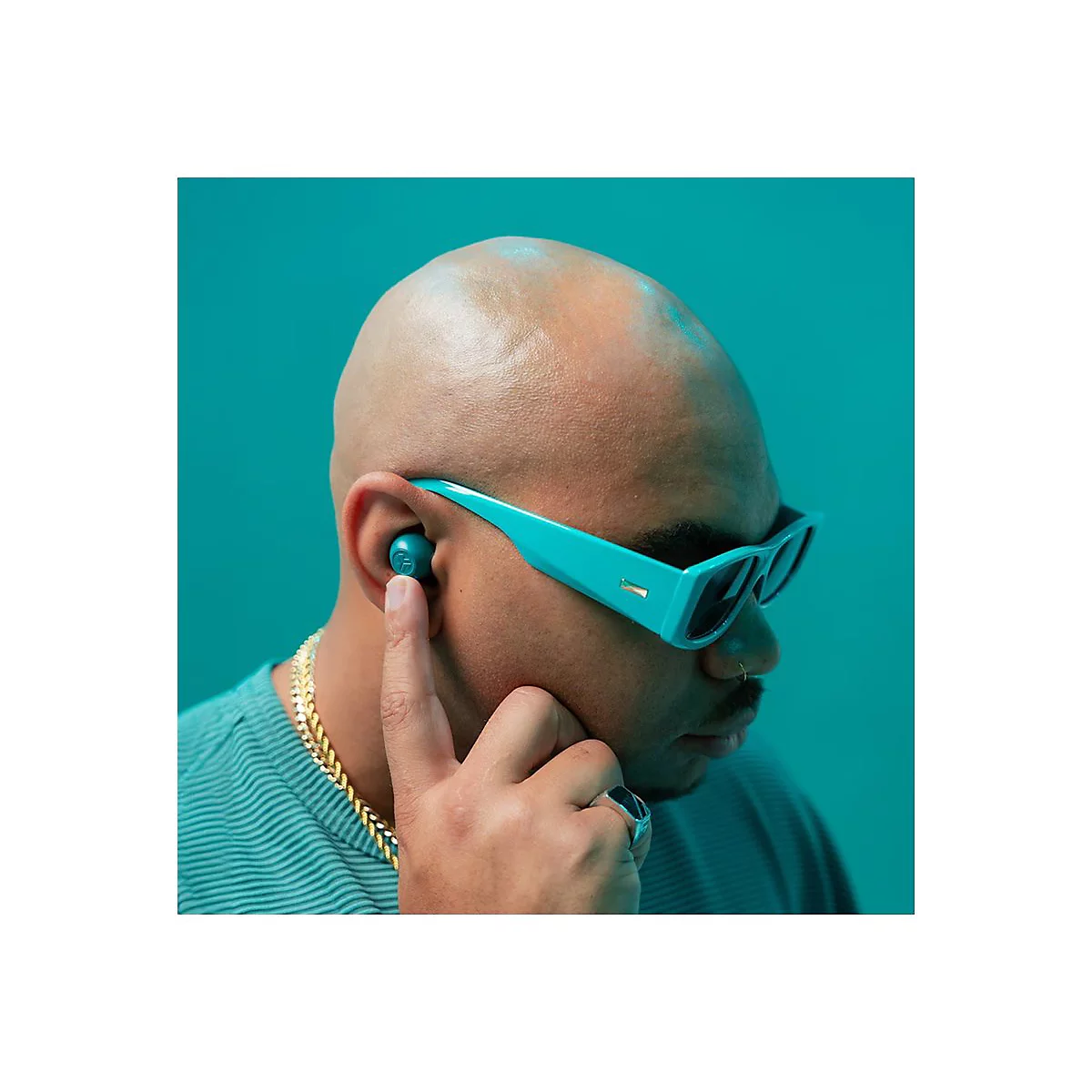 Un homme avec des lunettes de soleil et des écouteurs touche un écouteur. Fond bleu et lumineux.