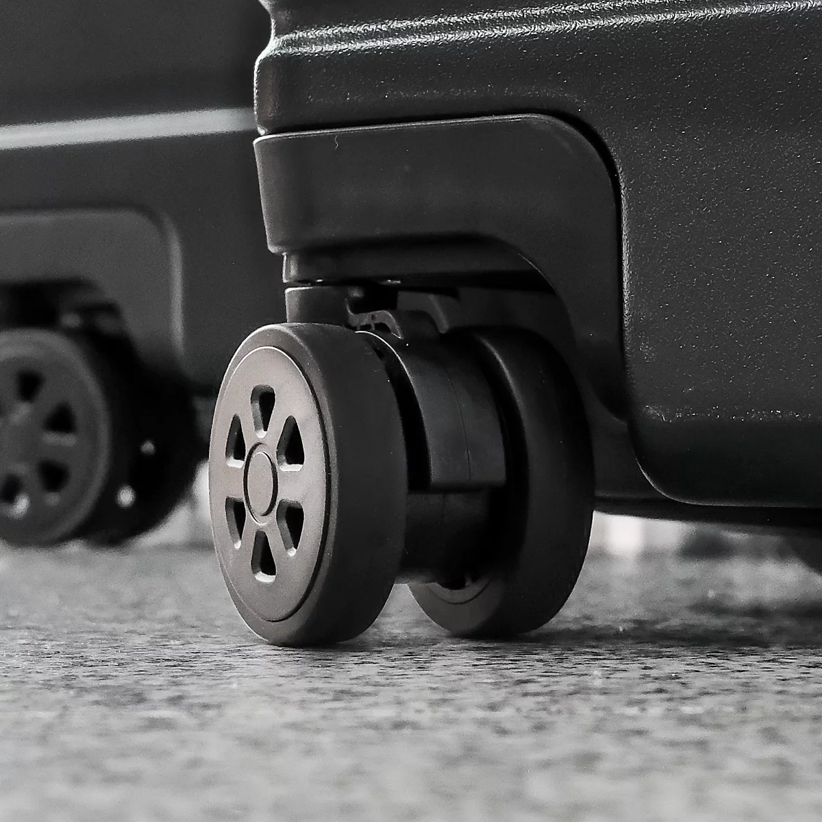Gros plan sur les roues d'une valise noire sur une surface grise. L'accent est mis sur les roues.