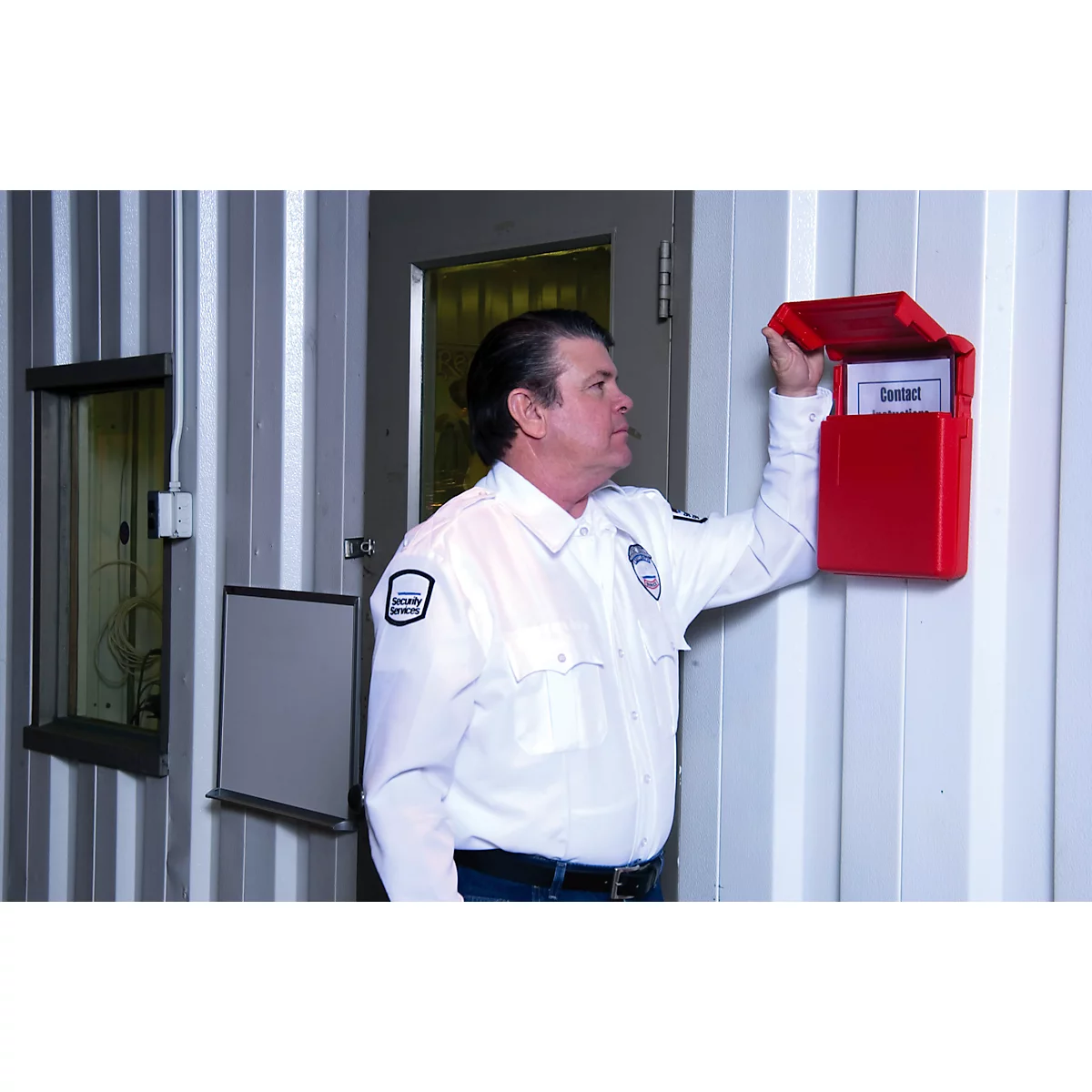 Ein Mann in Uniform öffnet einen roten Briefkasten an einer Wand. Auf dem Zettel im Briefkasten steht "Kontakt".