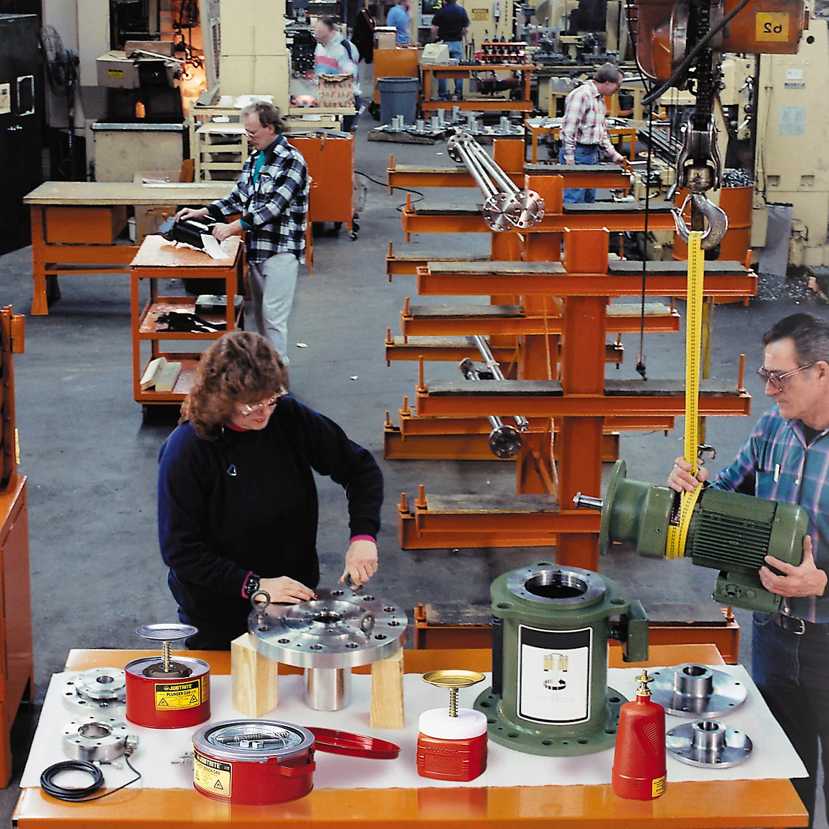 Workshop scene with workers handling components. Various parts are on tables.