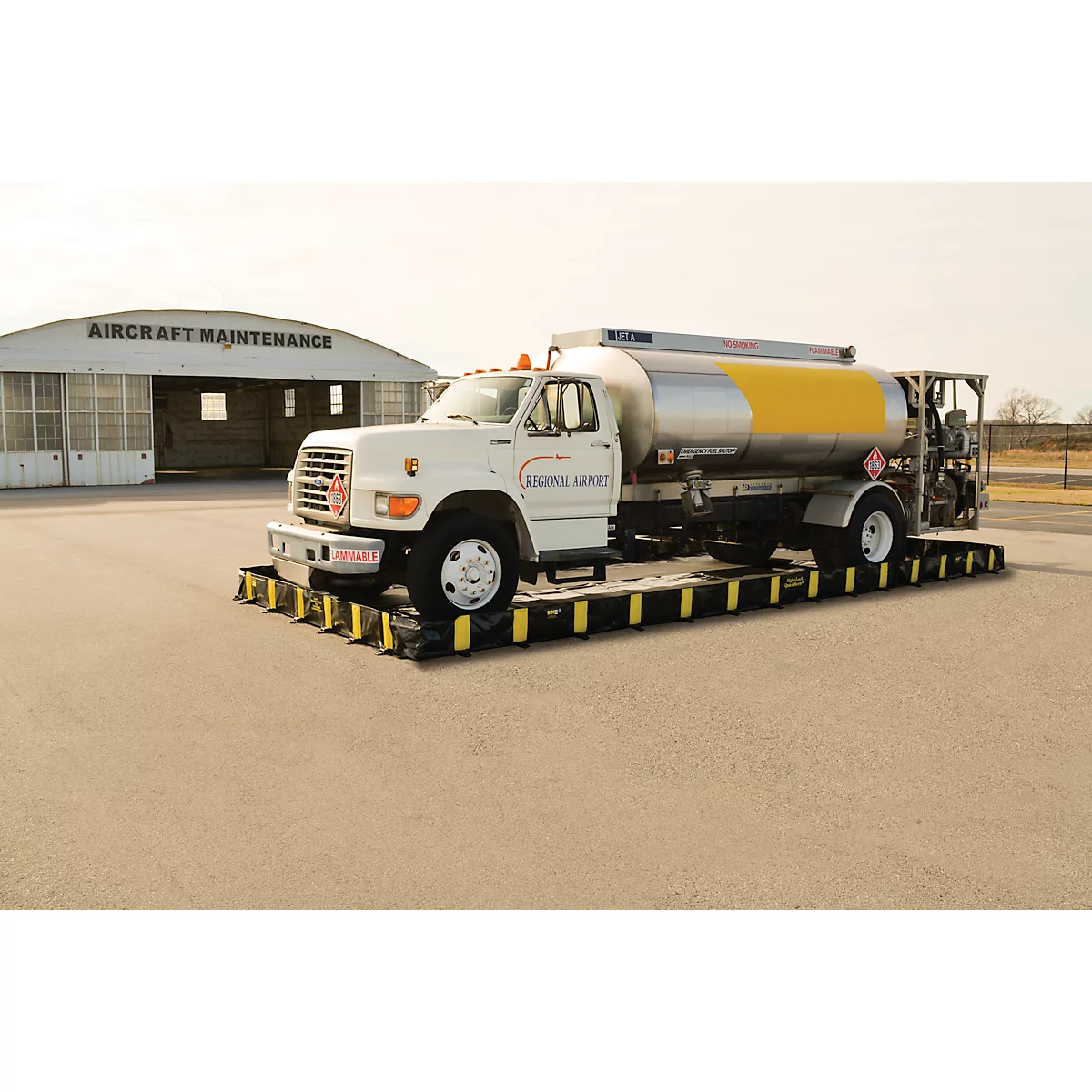 Tankwagen op een platform; op de achtergrond een hangar met opschrift "AIRCRAFT MAINTENANCE".