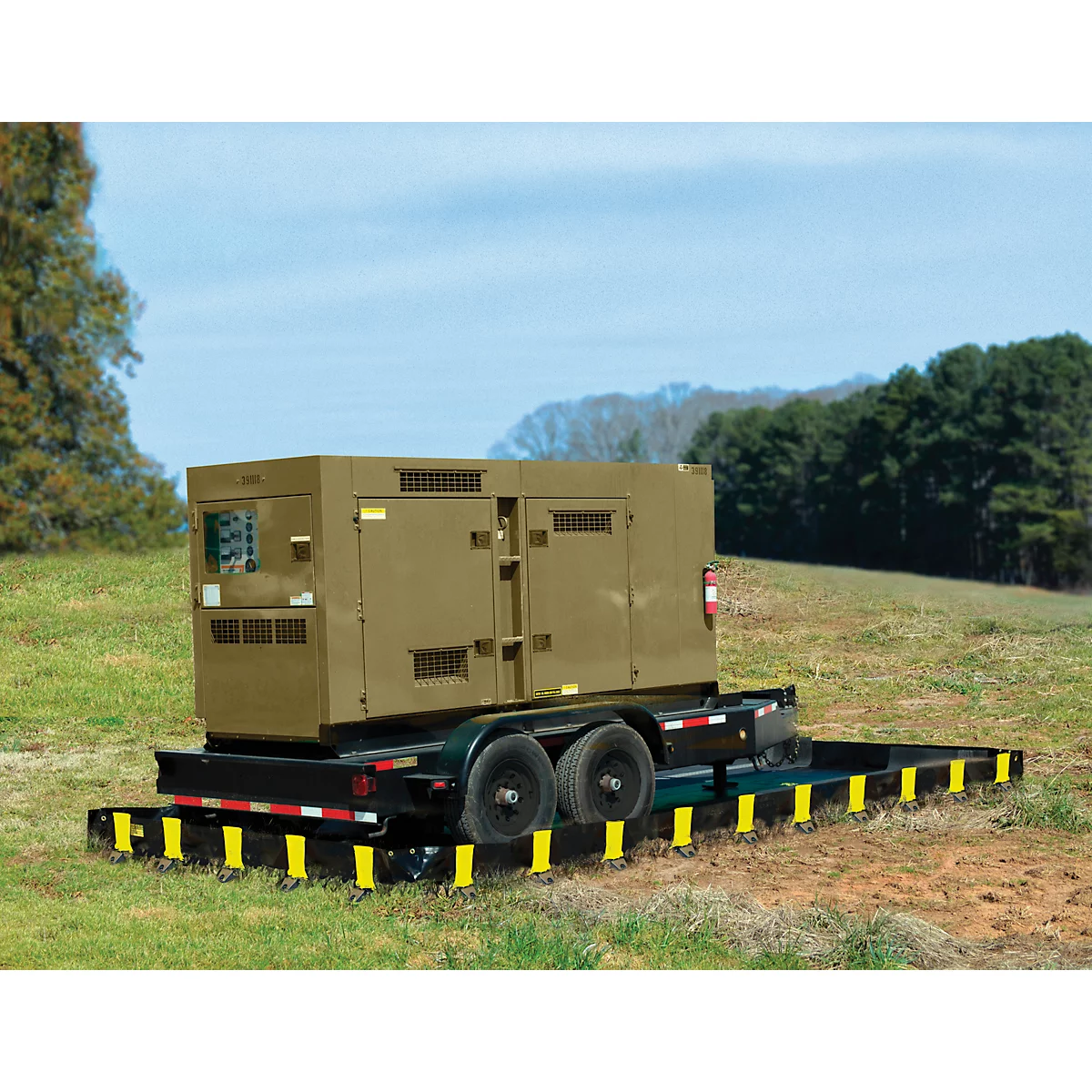 Een grote, beige generator op een aanhanger, staand in een weiland. Op de achtergrond bomen en een blauwe lucht.