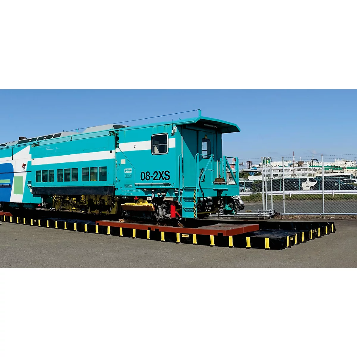 Turquoise trein staat op een zwart spoor. Blauwe lucht op de achtergrond.