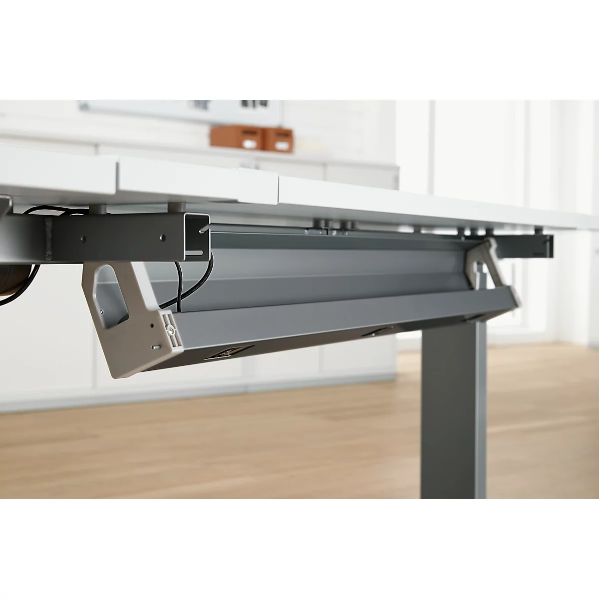 Grijs metalen compartiment onder een witte tafel, kabels zichtbaar.