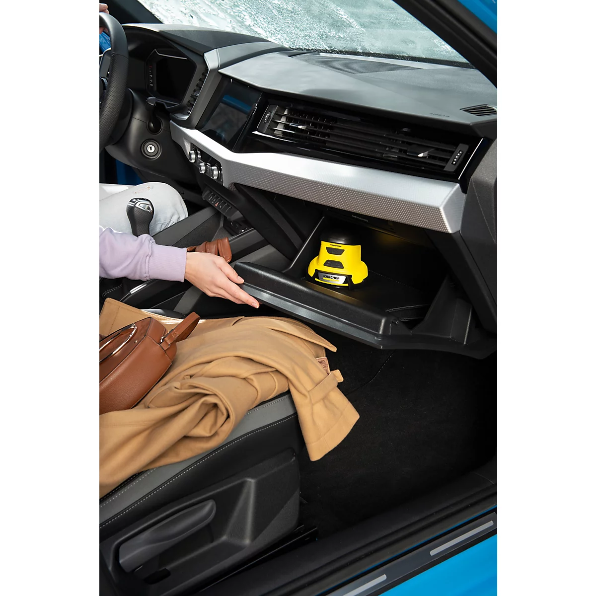 Een persoon opent het dashboardkastje van een blauwe auto. Binnenin staat een geel apparaat.