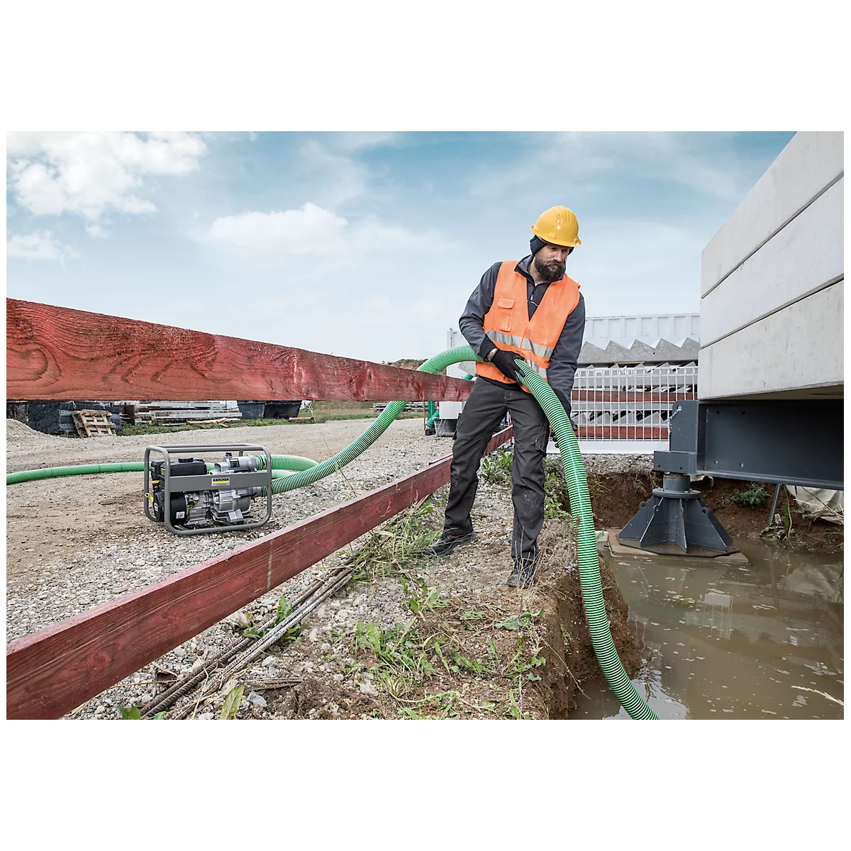 Een bouwvakker met een veiligheidsvest en helm houdt een groene slang vast en pompt water weg.