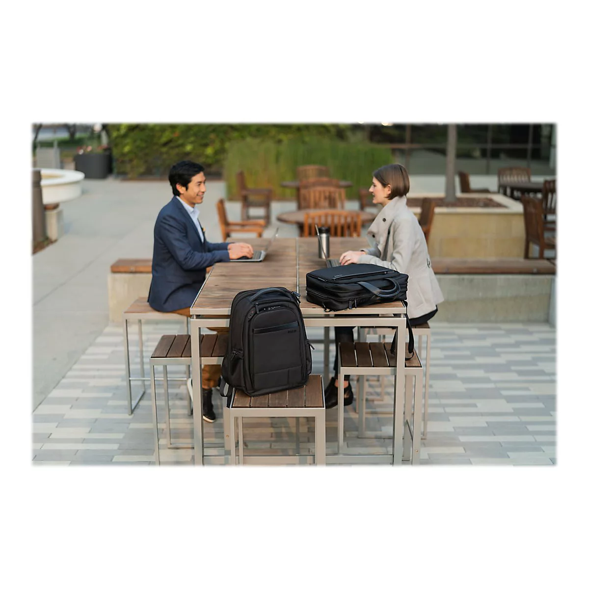 Zwei Personen sitzen an einem Tisch im Freien. Ein Mann tippt an einem Laptop, eine Frau sitzt ihm gegenÃ¼ber.