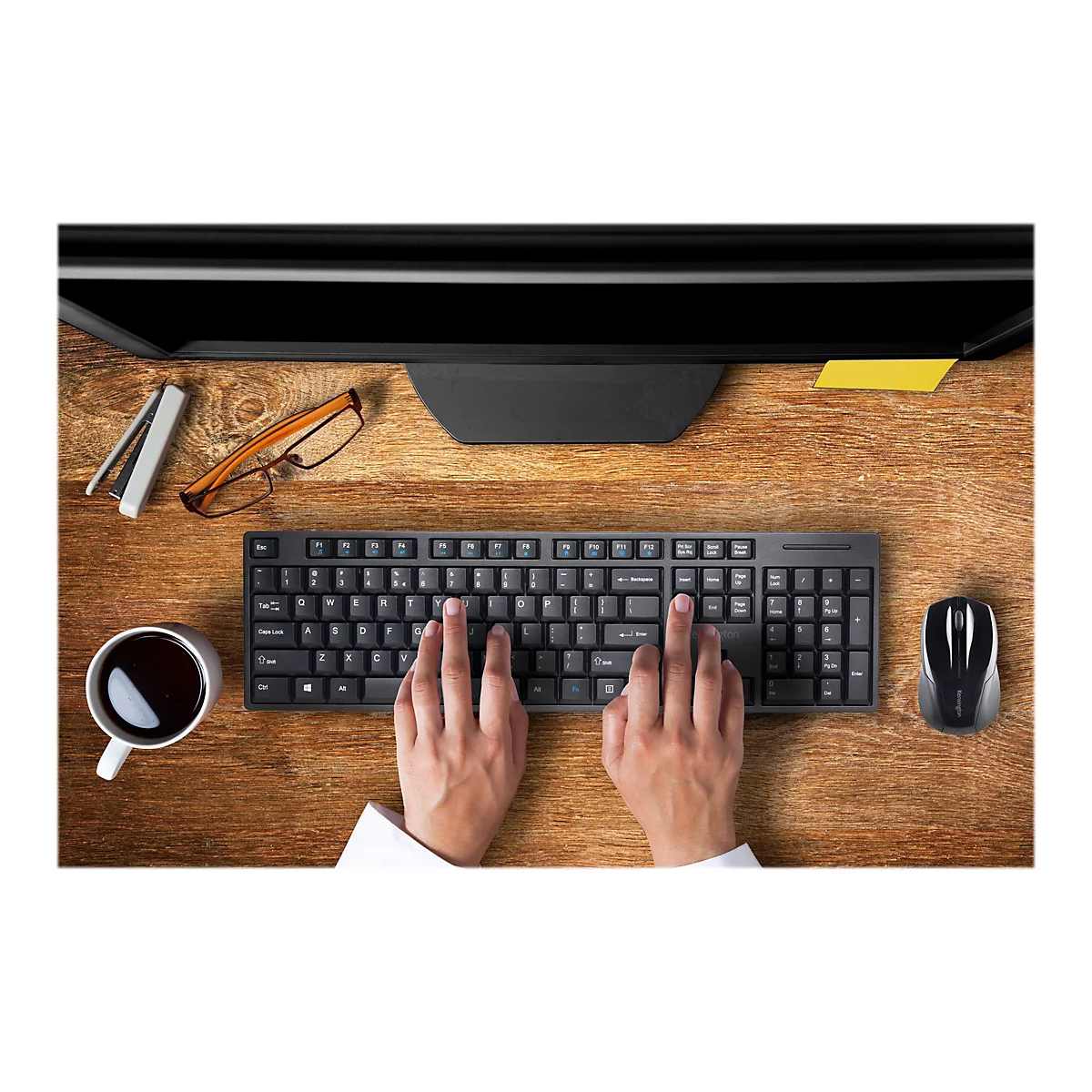 Draufsicht auf einen Schreibtisch mit Computer, Tastatur, Maus, Kaffeetasse und HÃ¤nden, die tippen.