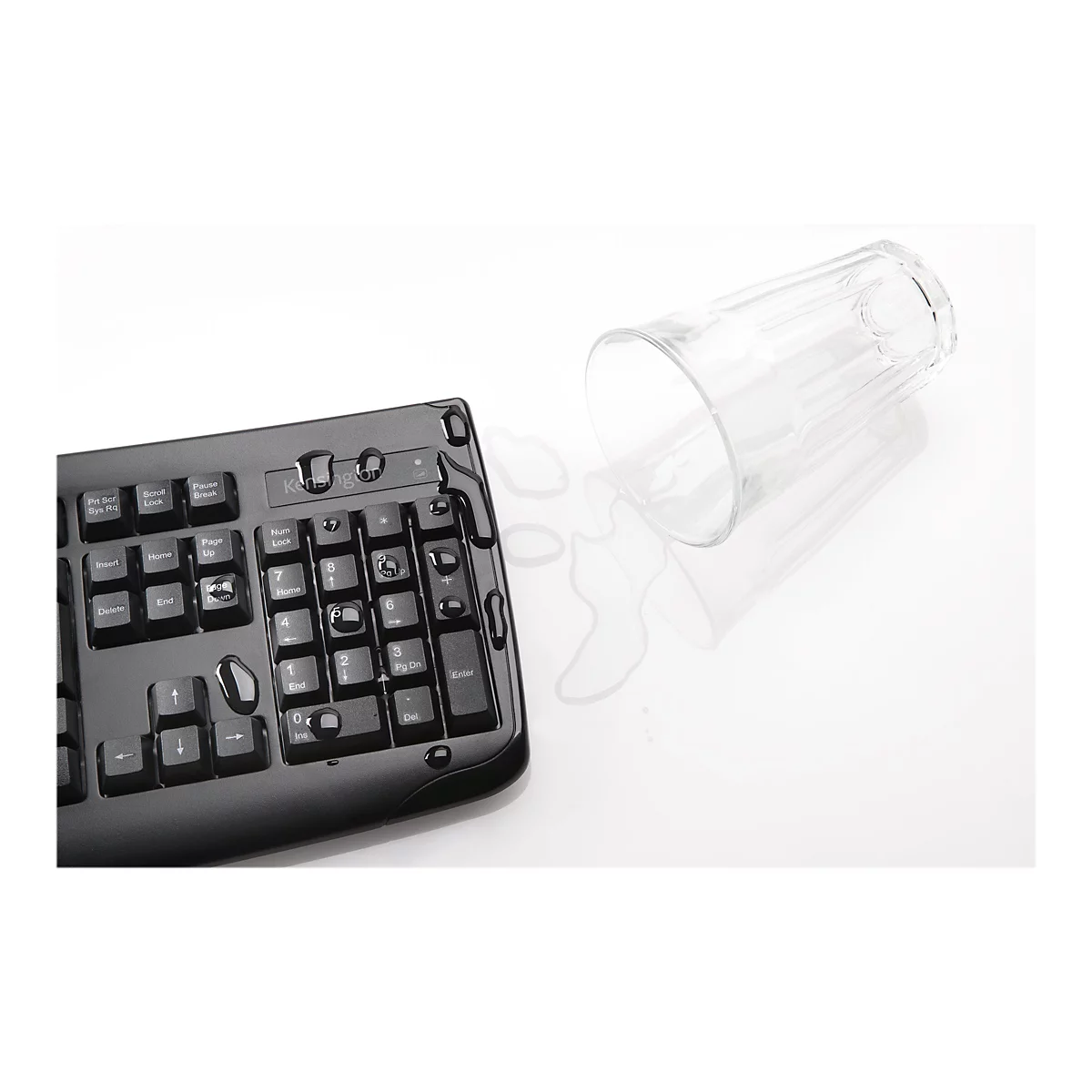 Schwarze Tastatur mit verschÃ¼ttetem Wasser. Daneben liegt ein umgekipptes Glas.