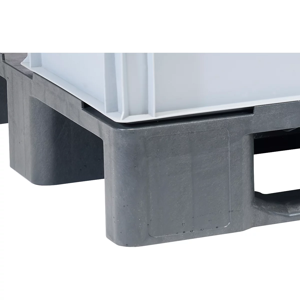 Gros plan d'une palette en plastique gris supportant un conteneur blanc. La palette a des pieds rectangulaires et des ouvertures.