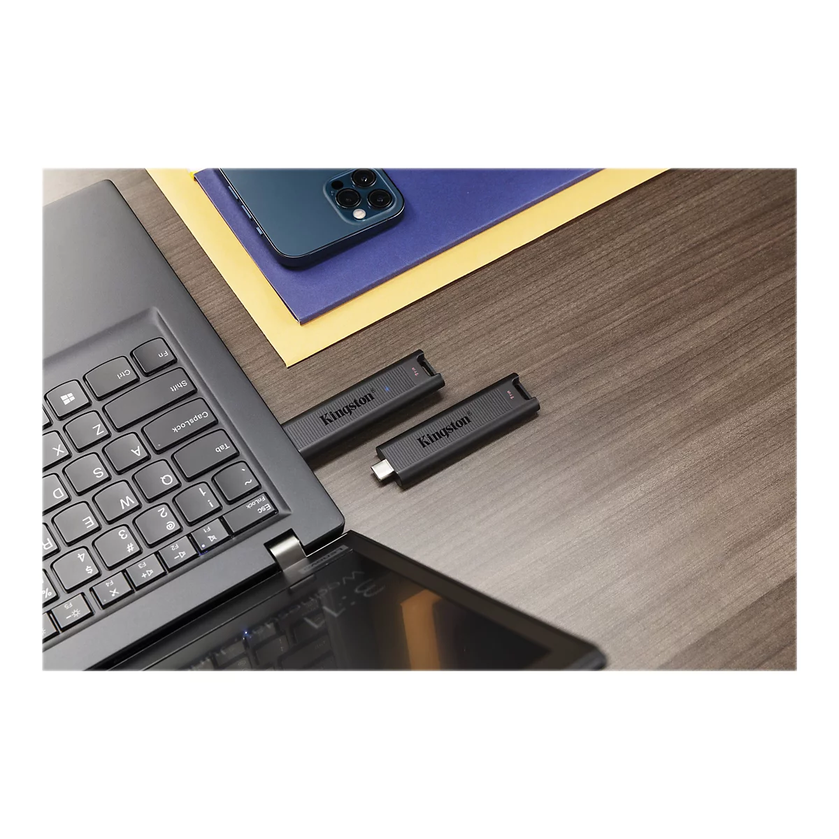 Schwarzer USB-Stick mit Kingston-Logo steckt in einem Laptop. Daneben ein weiteres Exemplar. Auf dem Tisch liegen Notizpapier und ein Smartphone.