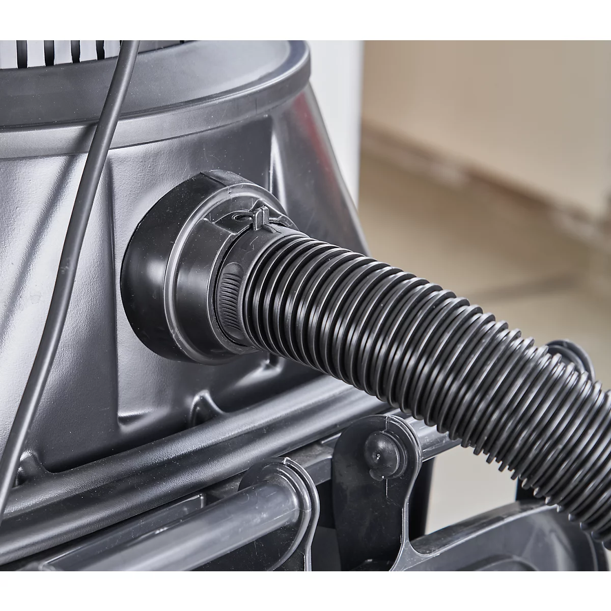 Gros plan d'un tuyau d'aspirateur noir attaché à un appareil gris.