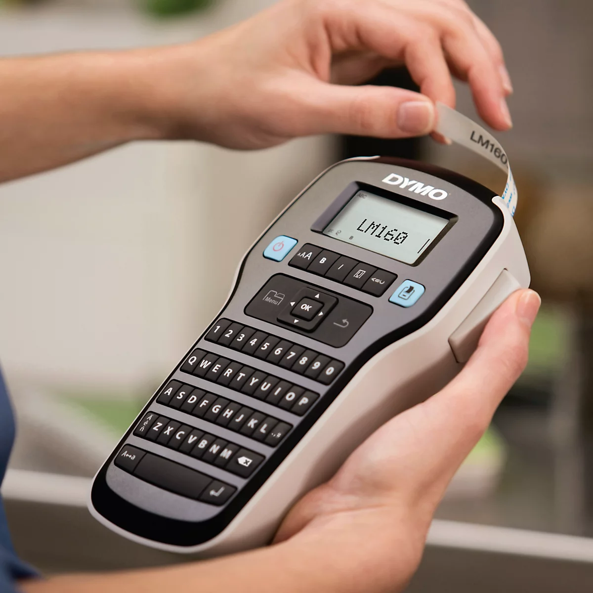 Une personne tient une étiqueteuse portable Dymo LM160 et tire une étiquette fraîchement imprimée.