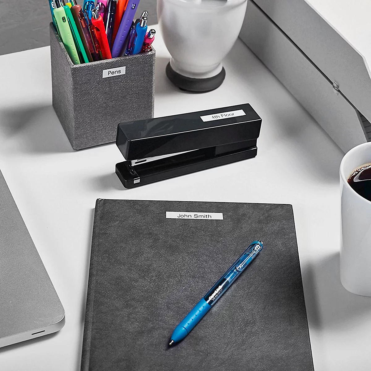 Bureau rangé avec porte-stylo étiqueté, agrafeuse, carnet et une tasse de café.