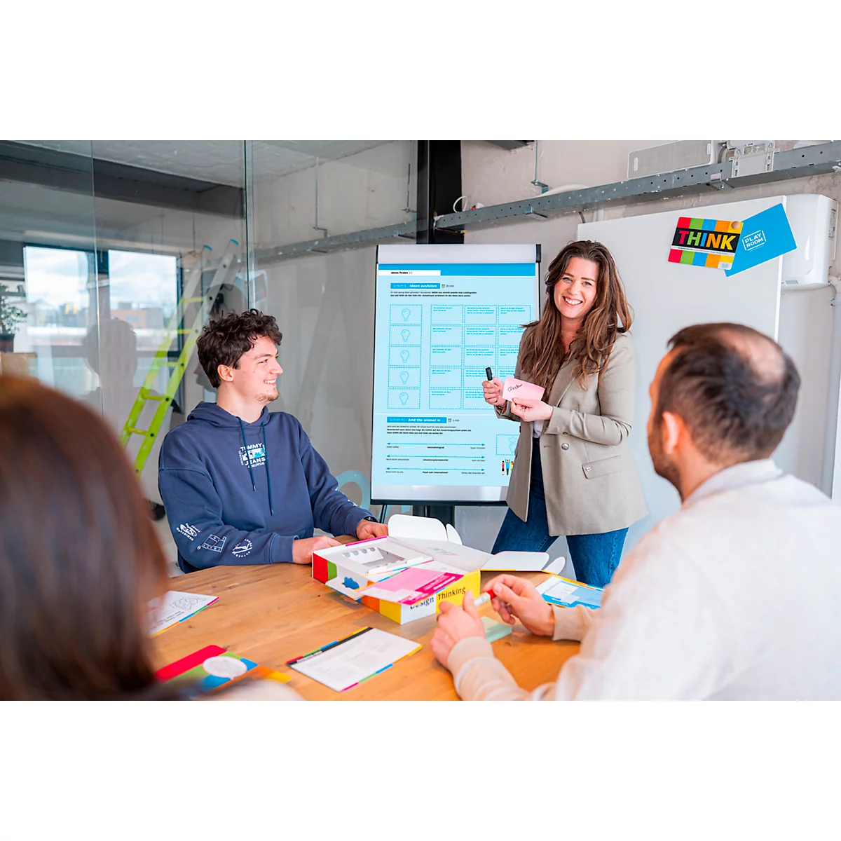 Une femme présente un tableau de conférence à une équipe. Tous les participants sont dans une salle de réunion.