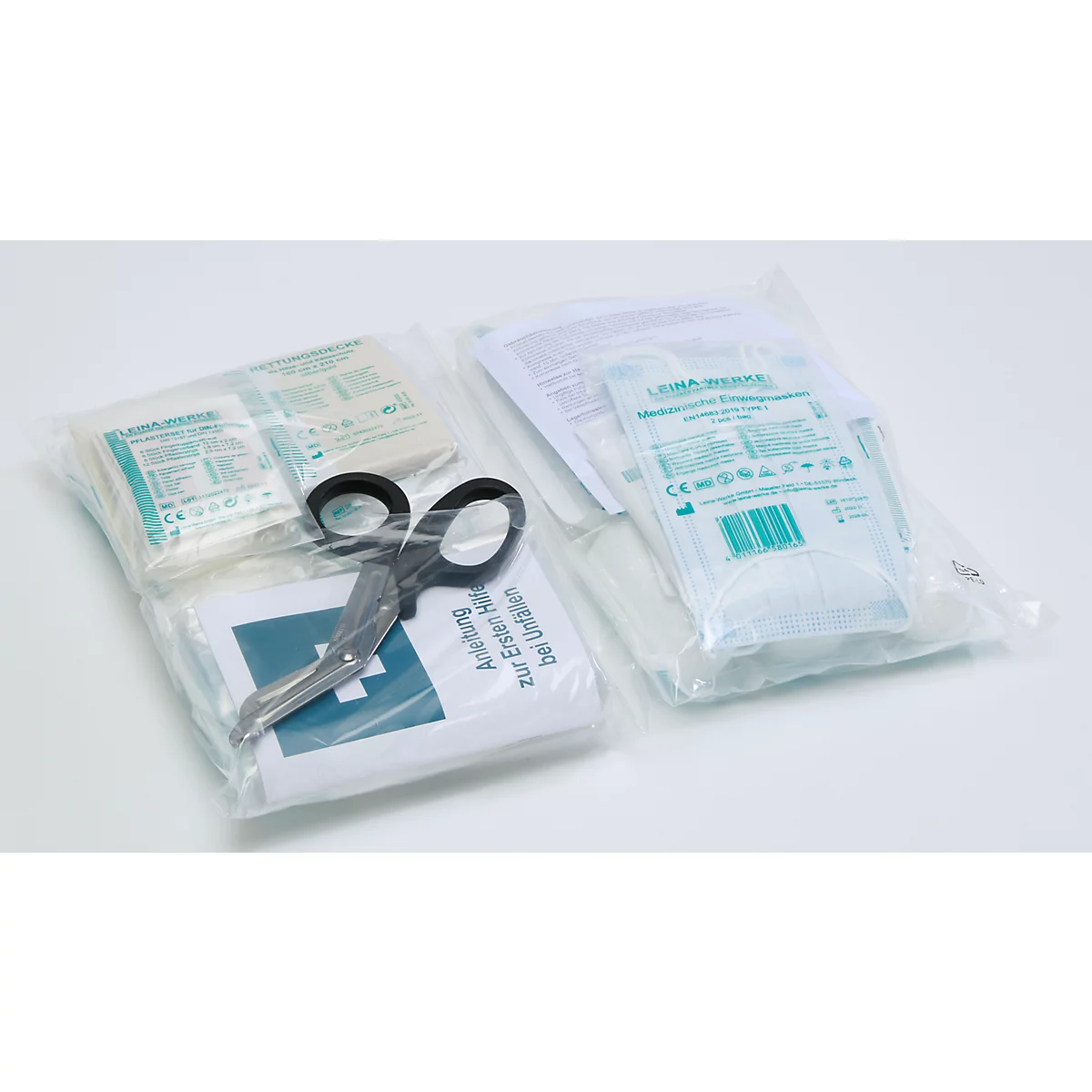 Deux trousses de premiers secours emballées dans du plastique avec des pansements et des ciseaux sur fond clair.