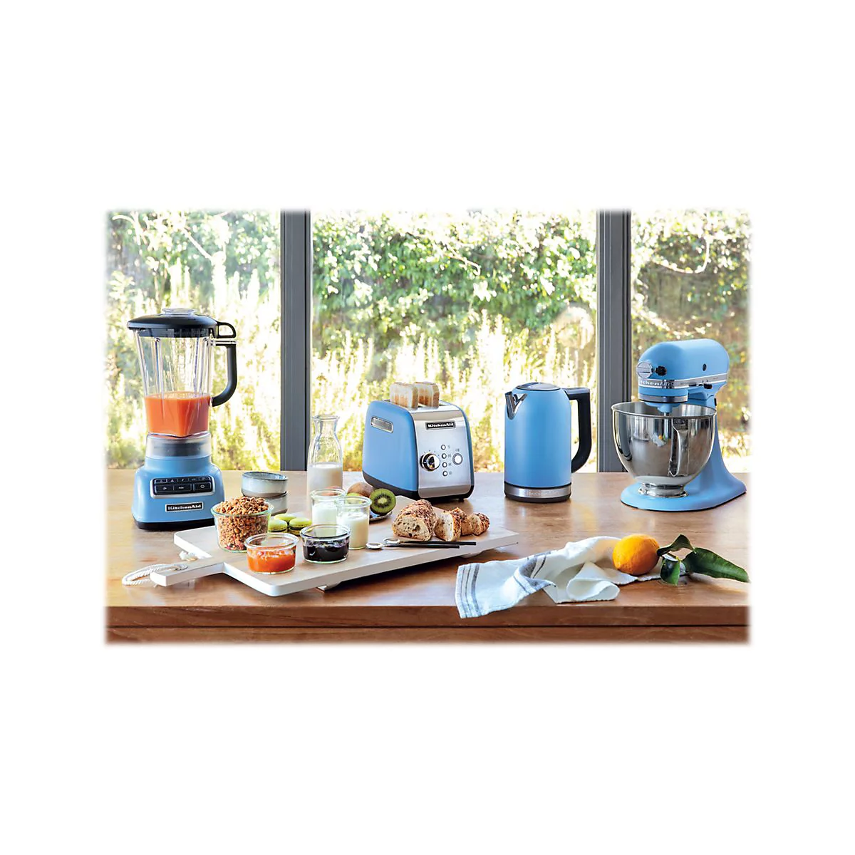 Blaues KitchenAid-Frühstücksset mit Mixer, Toaster, Wasserkocher und Küchenmaschine auf einem Holztisch.