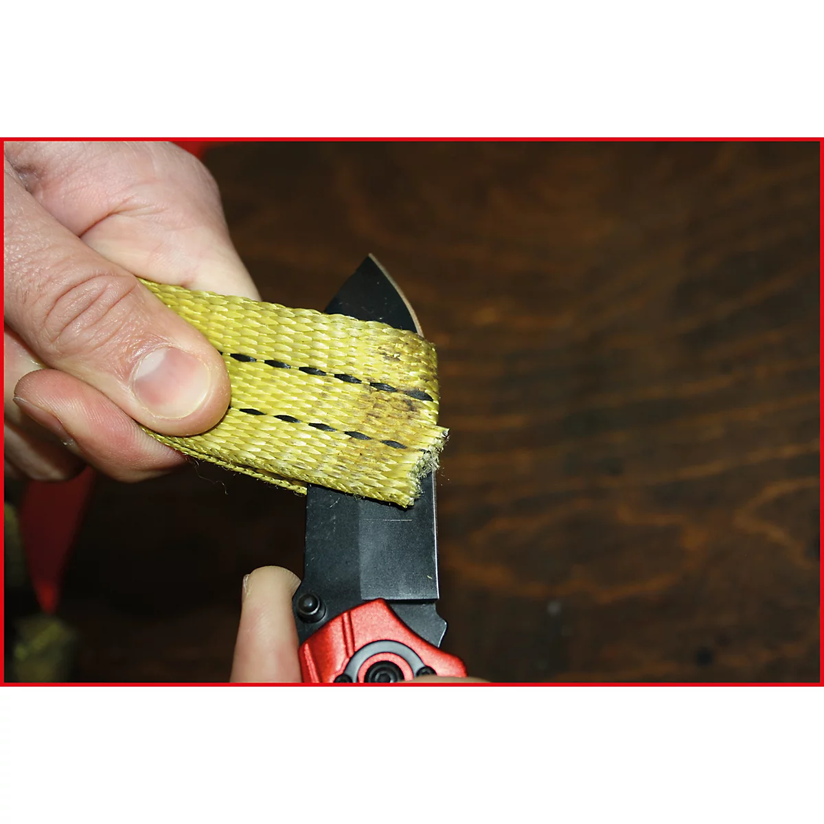 Nahaufnahme einer Hand, die ein gelbes Gurtband mit einem schwarzen Messer durchtrennt.