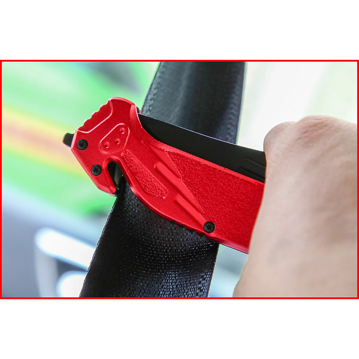 Rotes Notfallmesser schneidet einen schwarzen Sicherheitsgurt. Die Klinge und das Messer sind teilweise zu sehen.