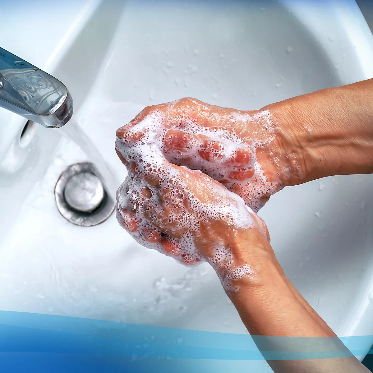 Hands being washed with soap in a sink, water flowing from the faucet.