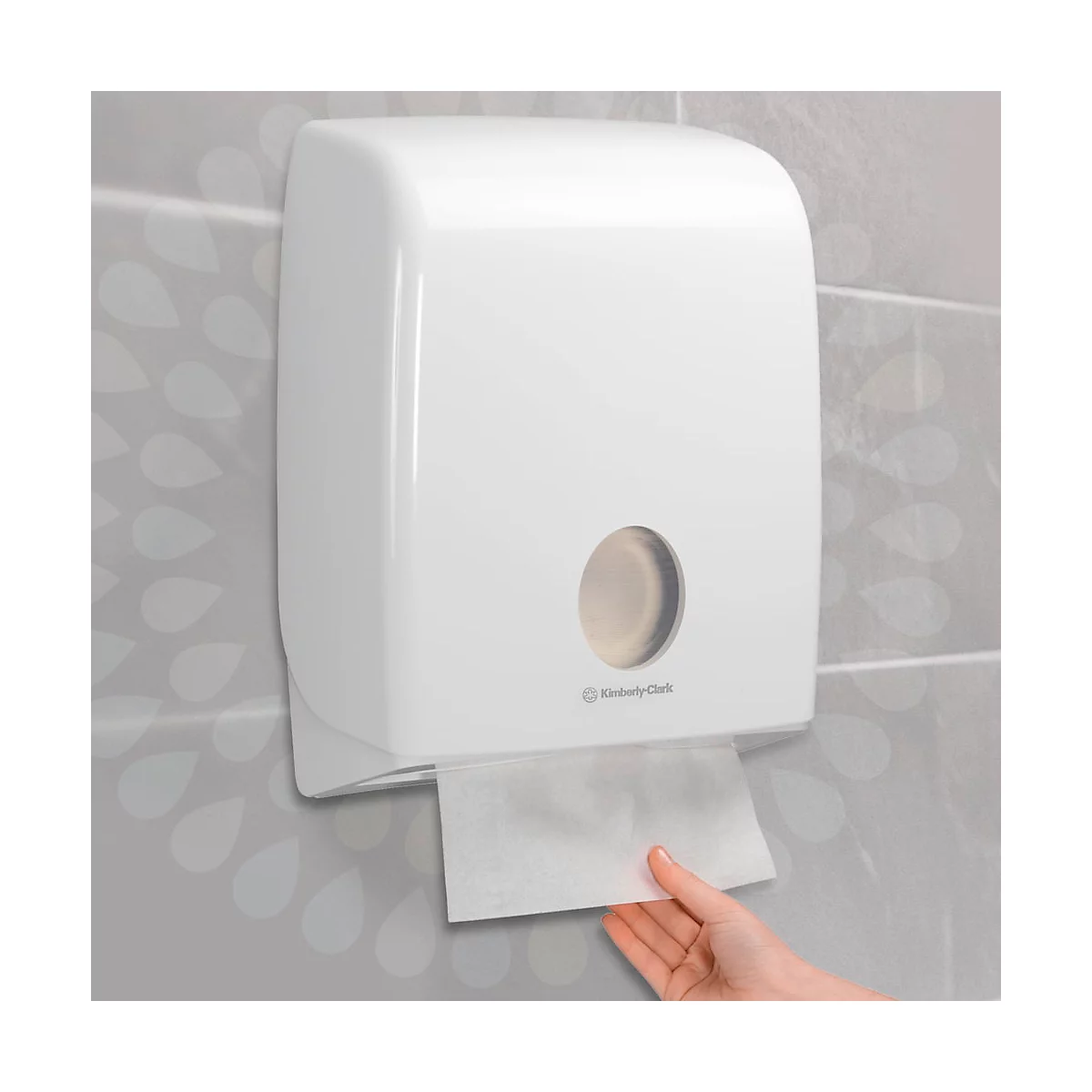 Dispensador de toallas de papel blanco en una pared gris. Una mano saca una toalla de papel.