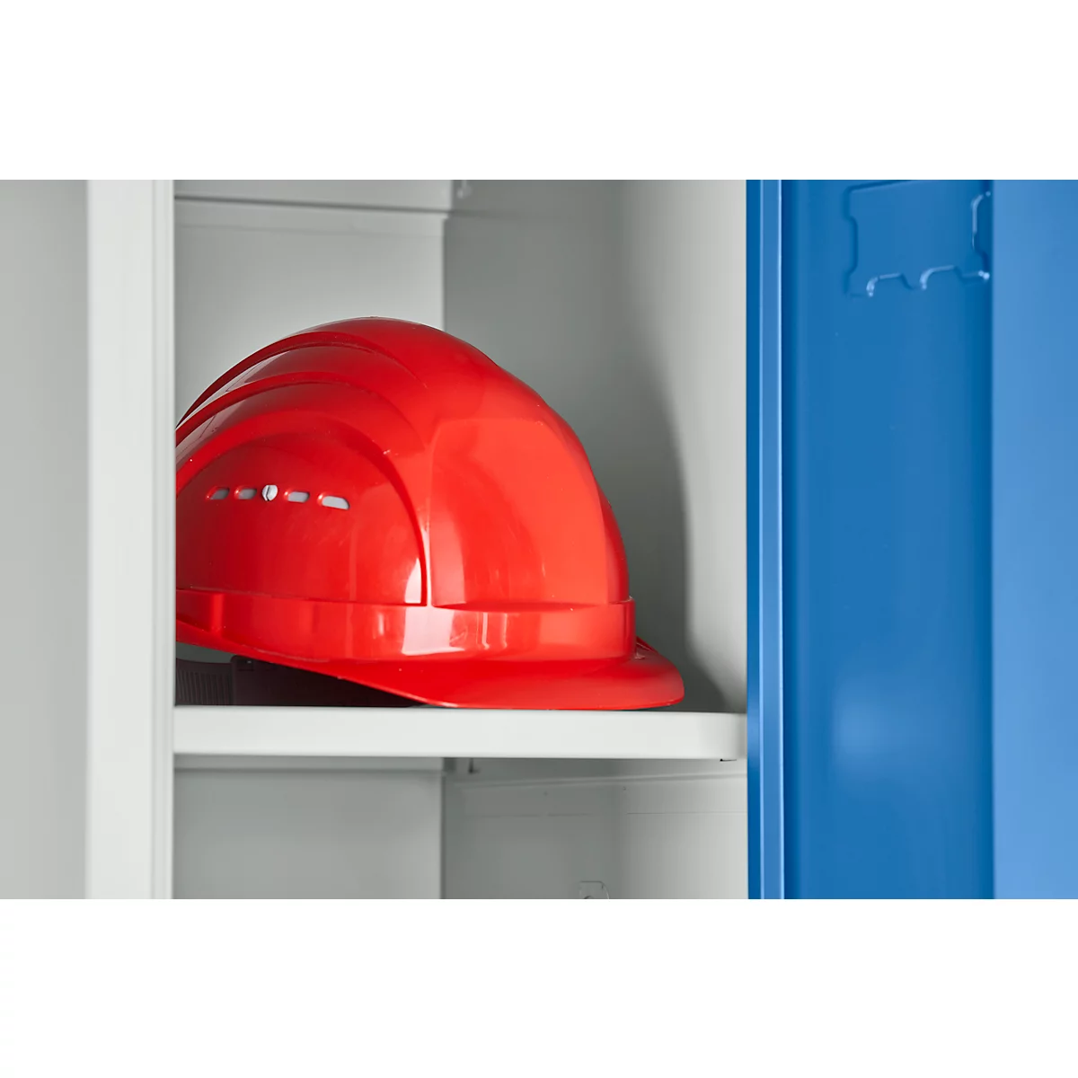 Roter Bauhelm in einem Schrank. Der Helm liegt auf einem Regal. Der Schrank ist blau und grau.