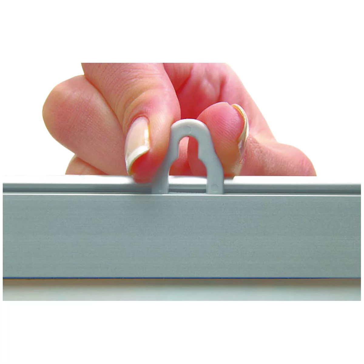 Eine Hand hält ein graues Hakenelement in einem grauen Rahmen fest. Der Finger hält das Element.