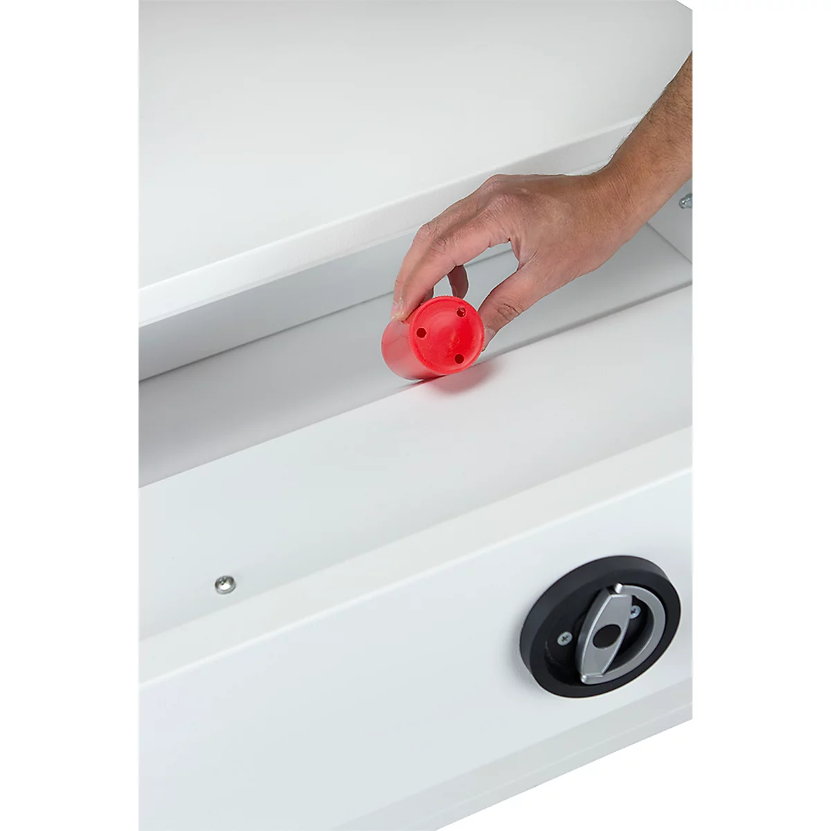 Hand houdt een rood plastic onderdeel vast. De achtergrond is wit en toont delen van een kast.