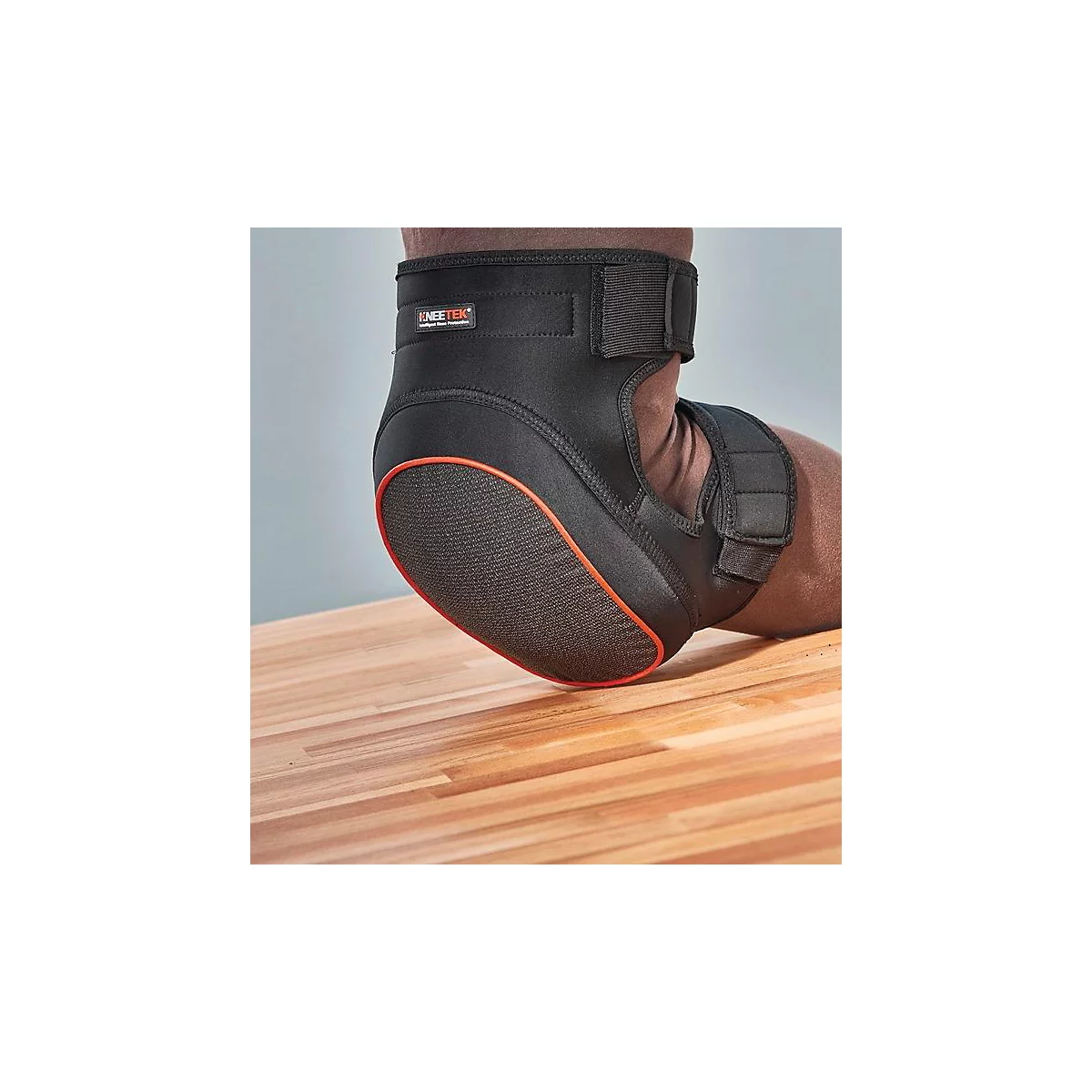 Genouillère noire sur jambe avec sangles velcro. Accents orange et logo du fabricant.