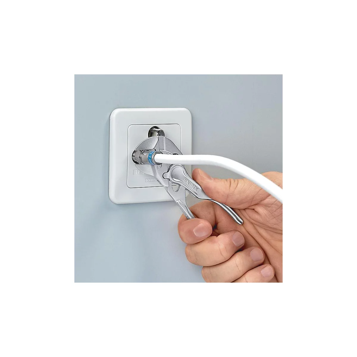 Une personne visse un câble coaxial dans une prise blanche avec une pince.