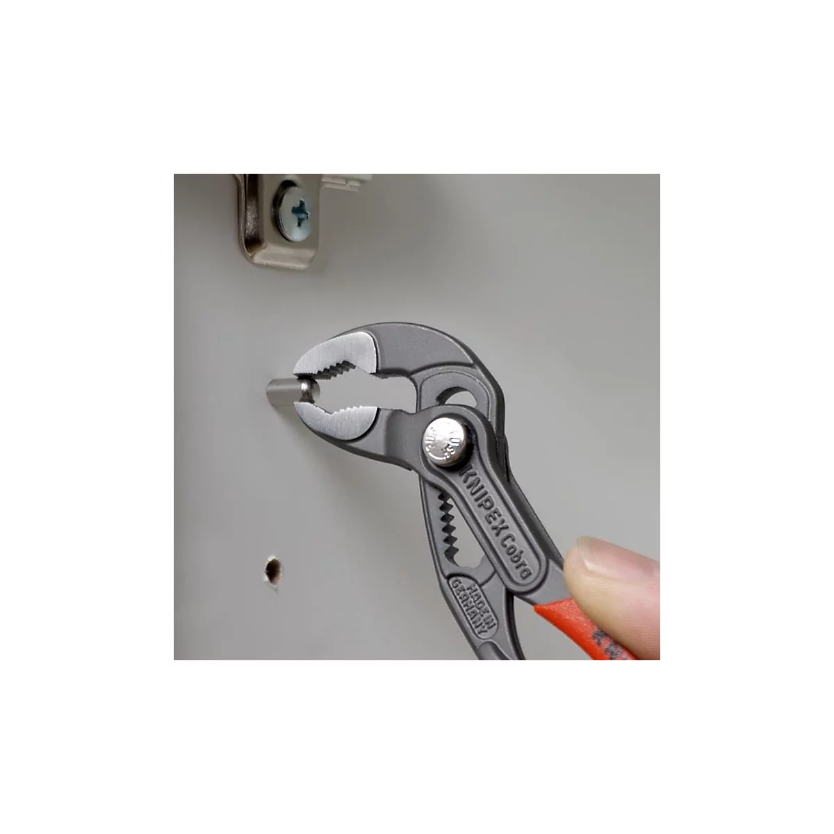 Eine Zange hält einen Stift, der in ein Loch gesteckt wird. Auf der Zange steht „KNIPEX Cobra“, rot abgesetzter Griff.