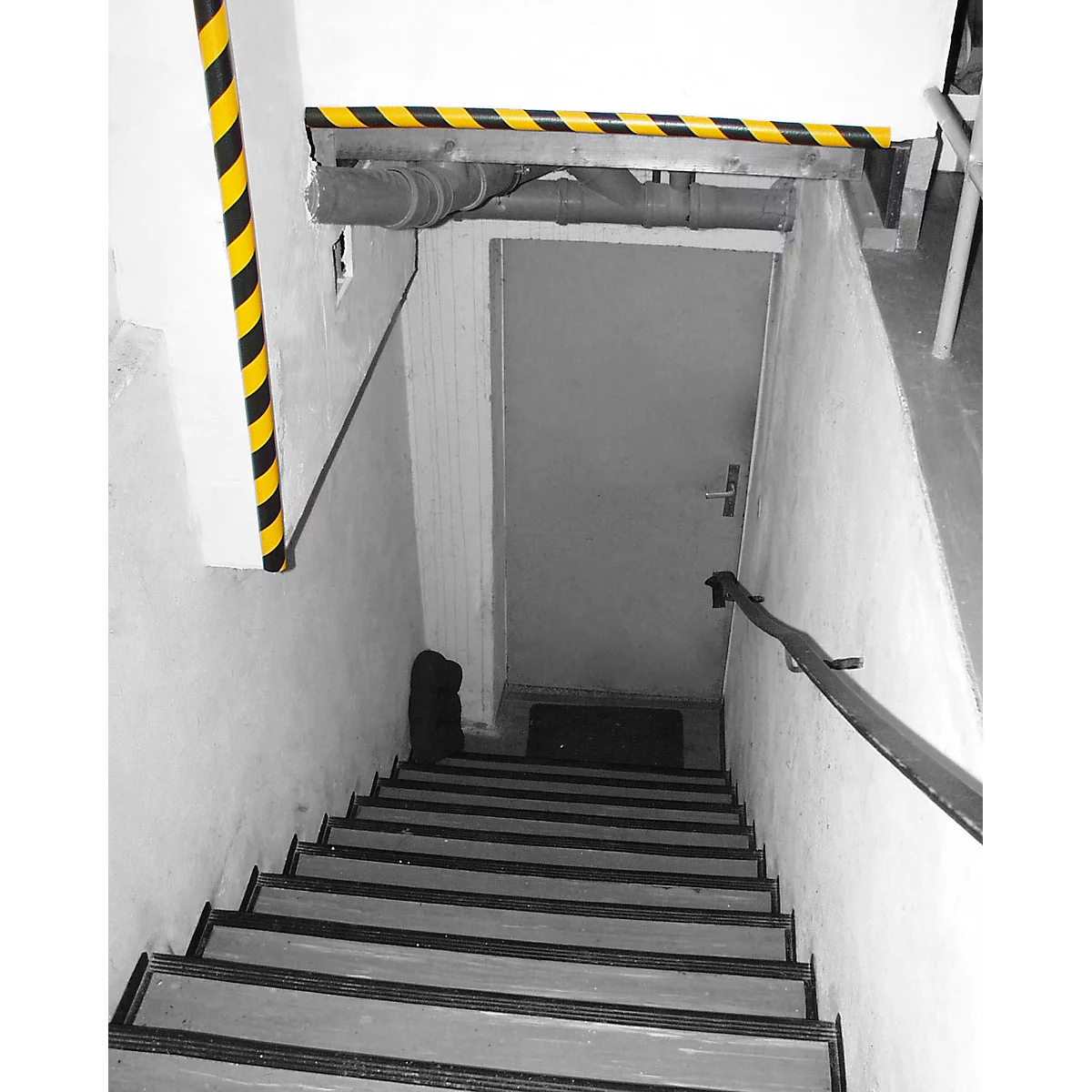 Stairwell with black and yellow hazard markings, gray door and handrail.