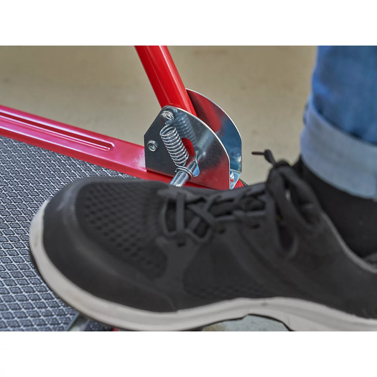 Nahaufnahme: Schwarzer Schuh auf einer roten Metallkonstruktion mit Feder und Fußstütze.