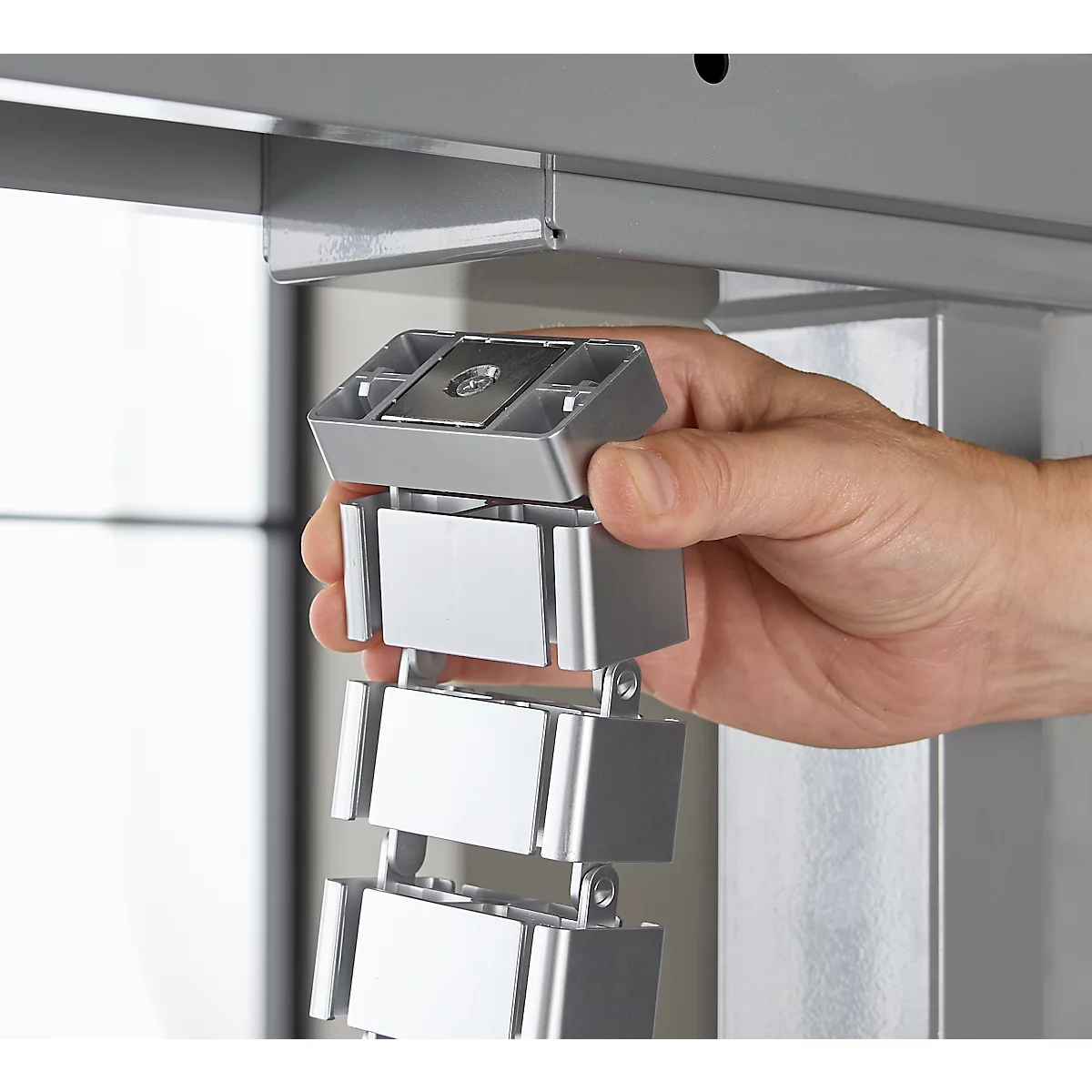 Nahaufnahme einer Hand, die ein silbergraues, aus mehreren Elementen bestehendes Verbindungsteil anbringt.