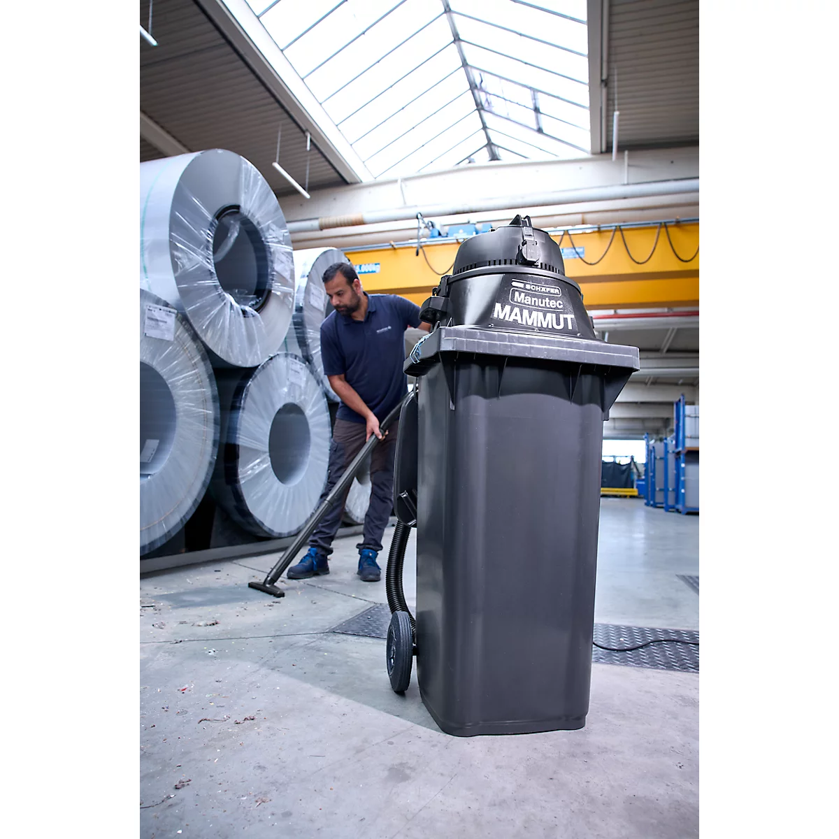 Ein Arbeiter reinigt mit dem Industriestaubsauger Marutec Mammut eine Lagerhalle mit Metallrollen.