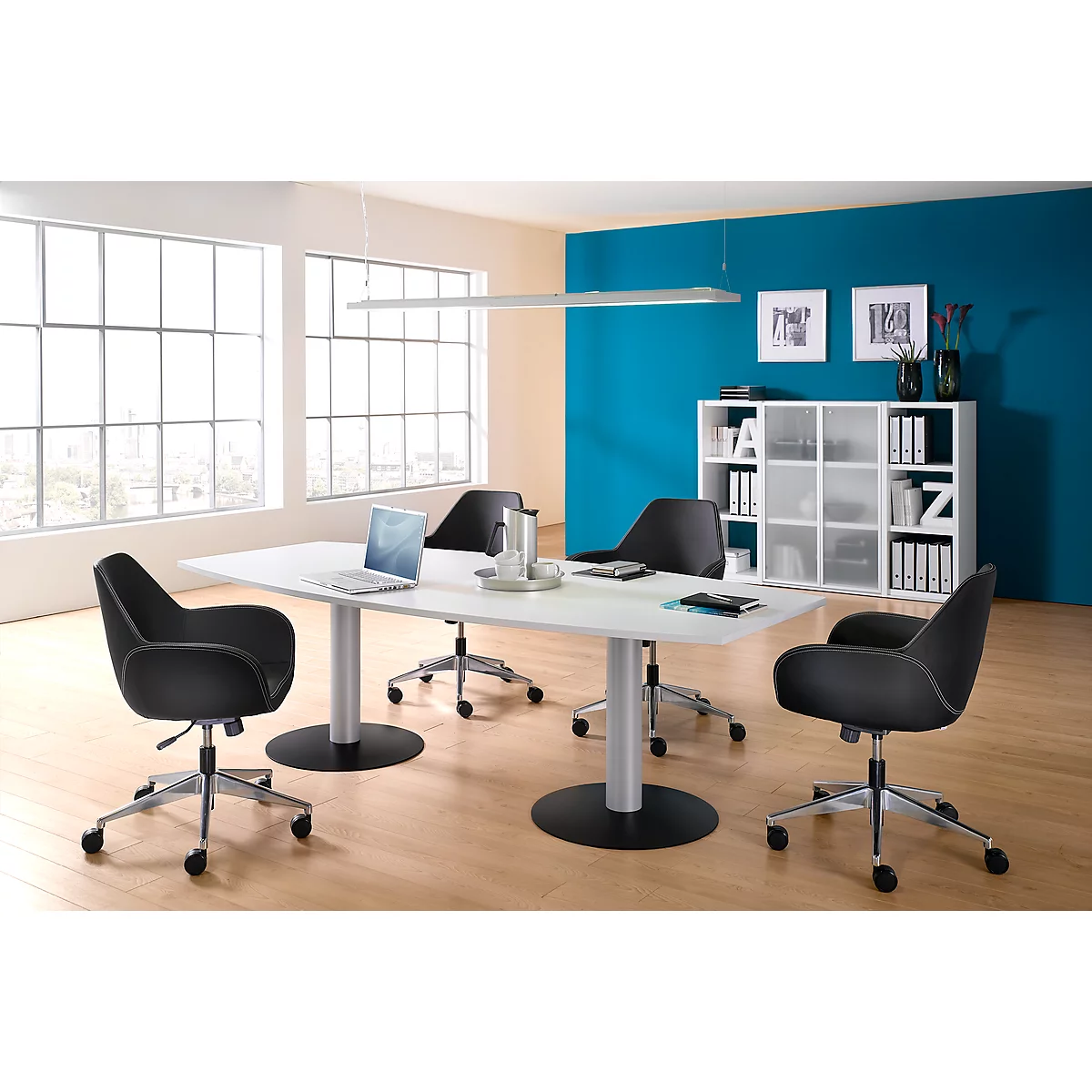 Büro mit Tisch, Stühlen und einem blauen Hintergrund. Ein Laptop liegt auf dem Tisch. Helle Fenster und Deckenlampe.