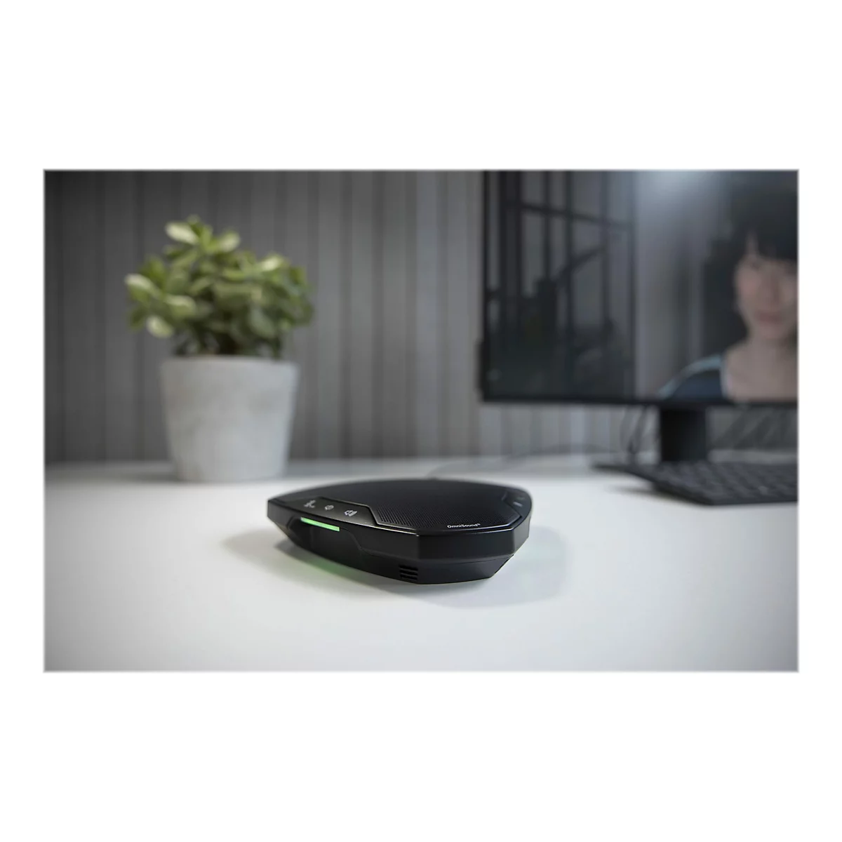 Schwarzes GerÃ¤t auf einem weiÃŸen Schreibtisch mit Pflanze im Hintergrund. Ein Monitor und Tastatur sind auch im Bild.