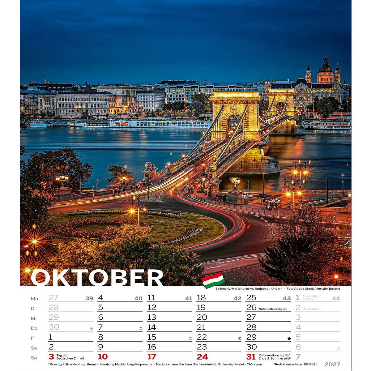 Vue sur le pont des Chaînes illuminé sur une rivière la nuit. En premier plan, le mois d'octobre. Une ville peut être vue à l'horizon.
