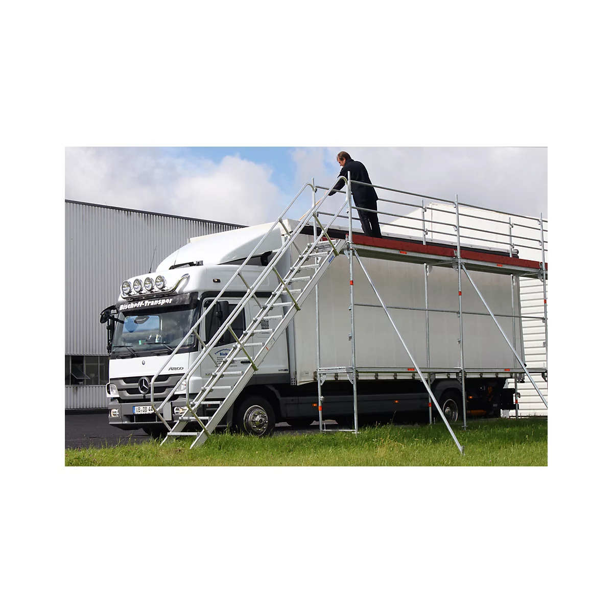 Man on scaffolding next to truck. Scaffolding with stairs to the truck roof. Inscription on truck: "Transport"