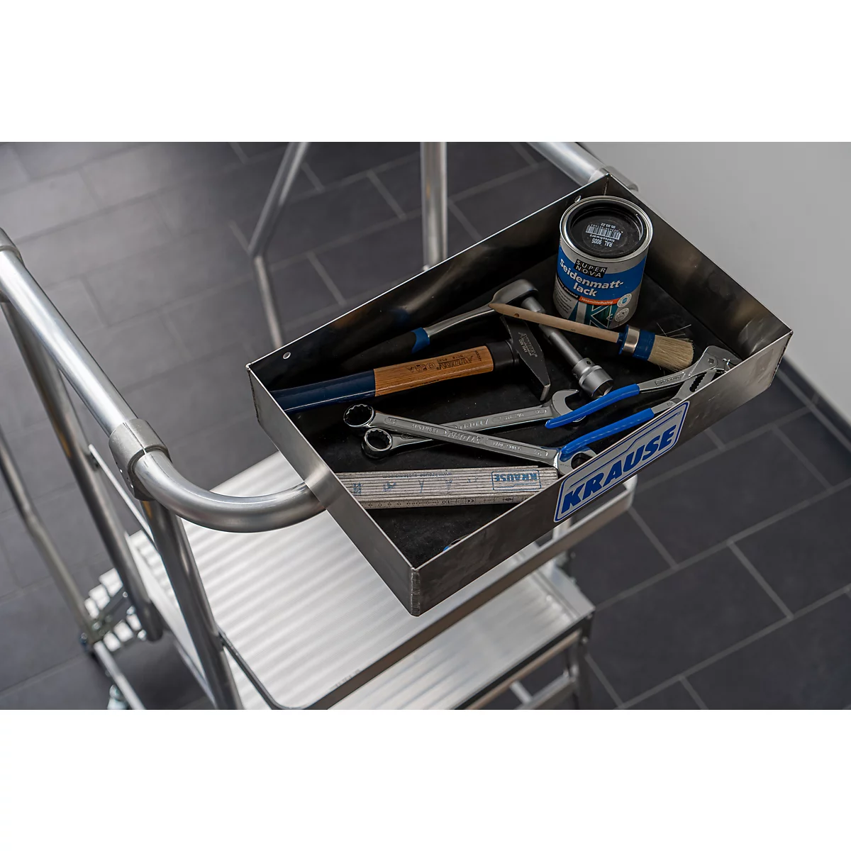 Metalen gereedschapskist met gereedschap op een zilveren trap. Gereedschap: hamer, moersleutels, kwast, verf. De vloer is betegeld.