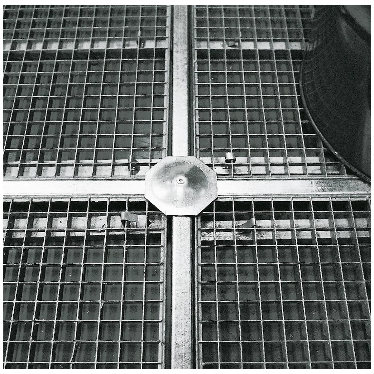 Draufsicht auf einen Metallrost mit achteckiger Abdeckung in der Mitte. Der Rost ist in Quadrate unterteilt.