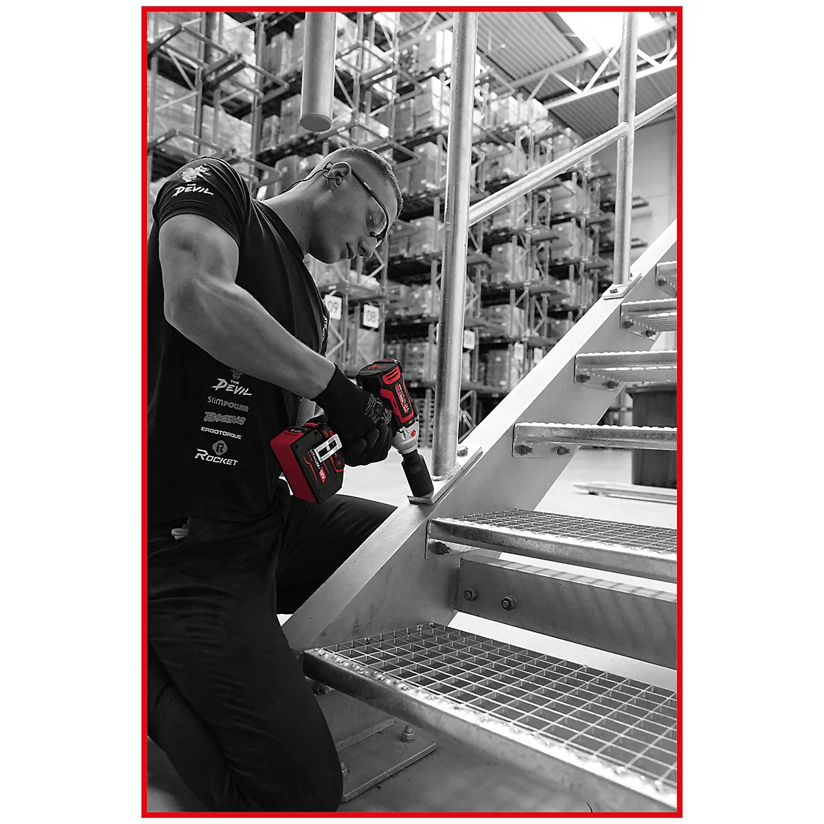 Handwerker in einem Lager verschraubt mit einem rot-schwarzen Schlagschrauber eine Metalltreppe.